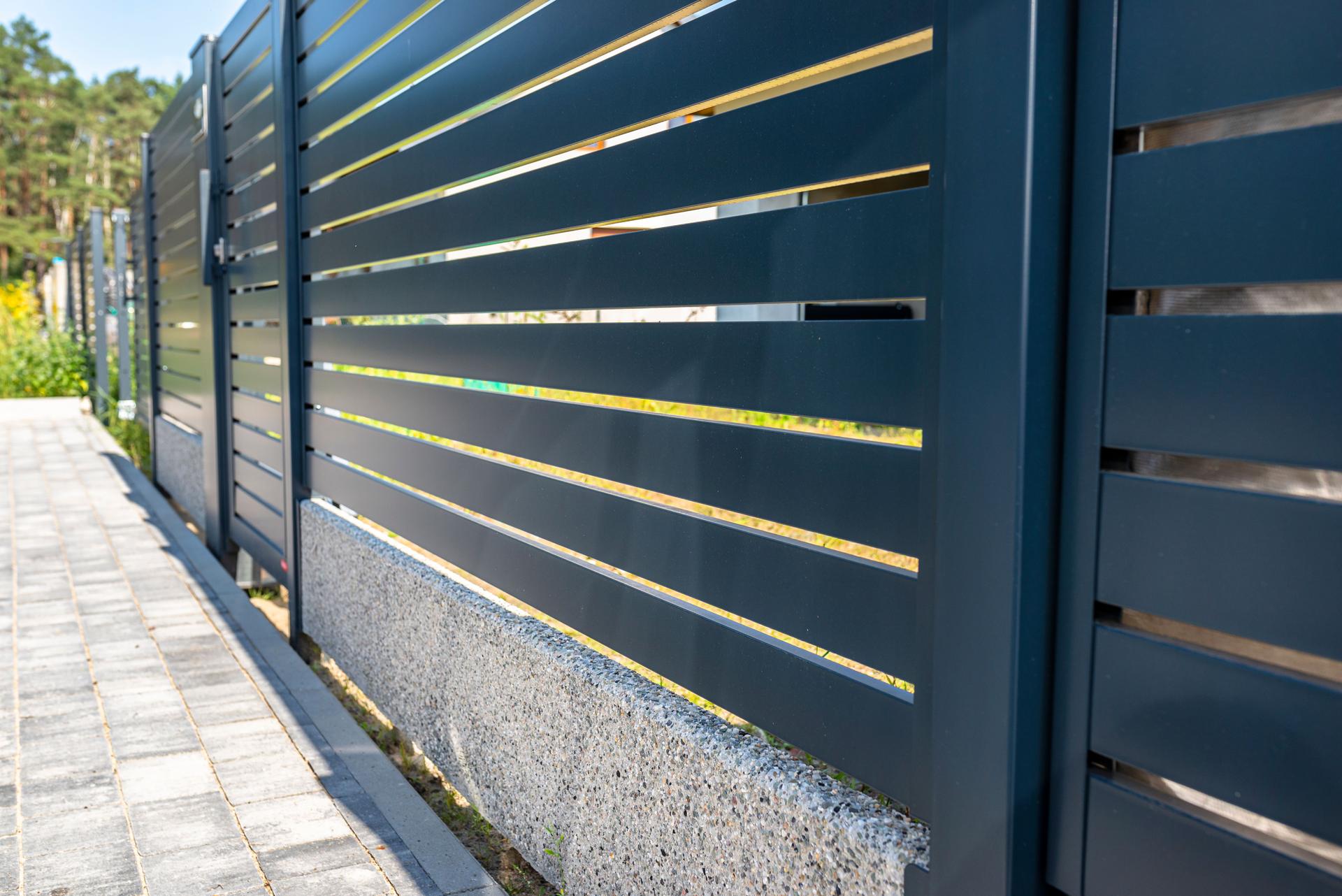 Modern panel fencing in anthracite color, visible spans and a wicket, forest in the background.