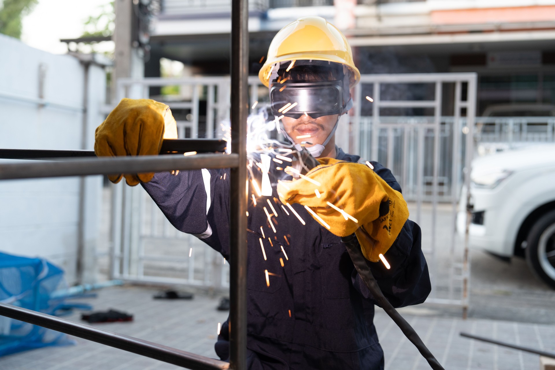 Asian worker wearing safety suit uses MIG welding machine.